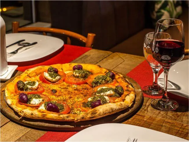 Pizza sobre a tábua de madeira, ao lado de uma taça de vinho tinto