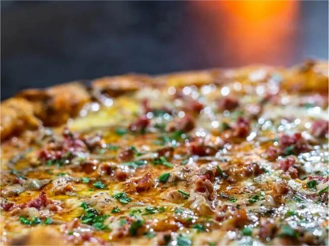 Close da pizza com queijo derretido e a luz do forno ao fundo